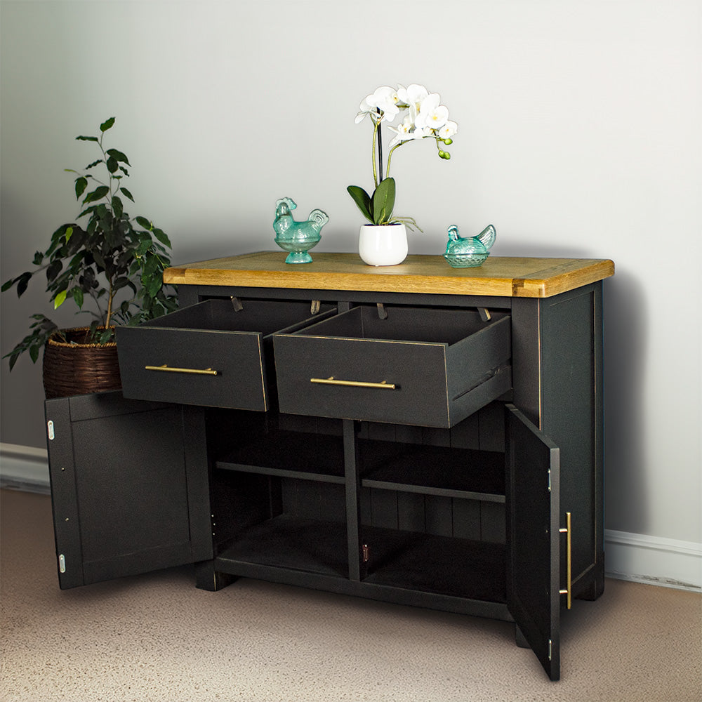 The front of the Cascais Oak-Top Two Drawer Buffet with its doors open. There are two blue glass ornaments on top with a pot of white flowers in between. There is a free standing potted plant next to the sideboard.