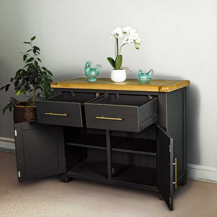 The front of the Cascais Oak-Top Two Drawer Buffet with its doors open. There are two blue glass ornaments on top with a pot of white flowers in between. There is a free standing potted plant next to the sideboard.