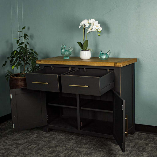 The front of the Cascais Oak-Top Two Drawer Buffet with its doors open. There are two blue glass ornaments on top with a pot of white flowers in between. There is a free standing potted plant next to the sideboard.