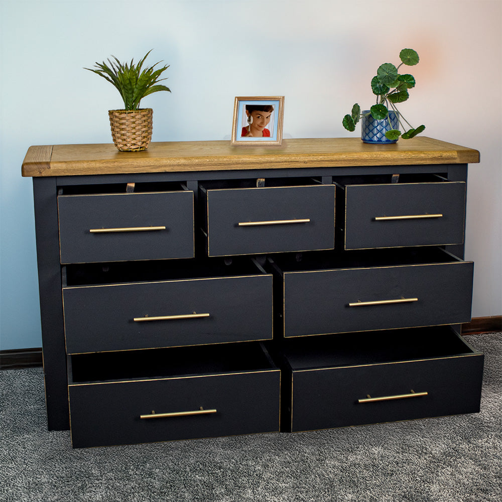 The front of the Cascais Oak Top 7 Drawer Lowboy (Black) with its drawers open. There are two blue glass ornaments in the middle on top with two potted plants on either side.