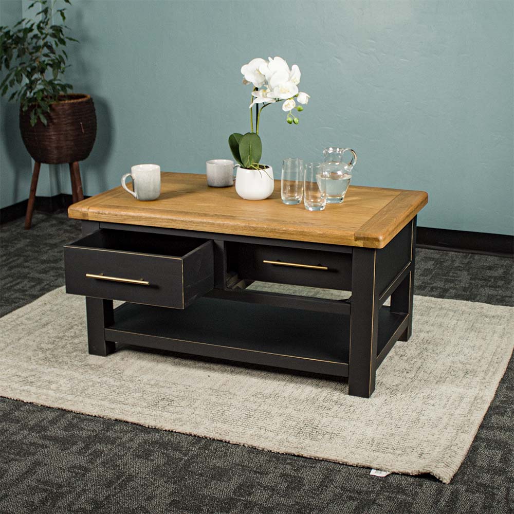 The front of the Cascais 2 Drawer Coffee Table with its drawers open. There is a pot of white flowers on top, two coffee mugs, a pitcher of water and two glasses on top.