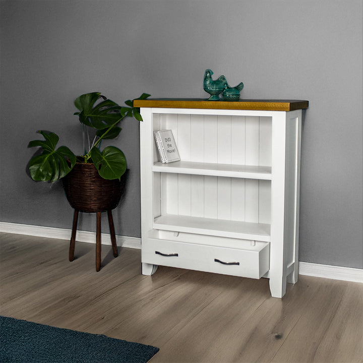 The front of the Felixstowe 1m Bookcase with its drawers open. There are two DVDs on the top shelf and two blue glass ornaments on top of the bookshelf. There is a free standing potted plant next to it.
