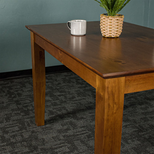 The side of the Hamilton Dining Table with Rimu Finish (1200mm), there is a coffee mug on top and a potted plant.
