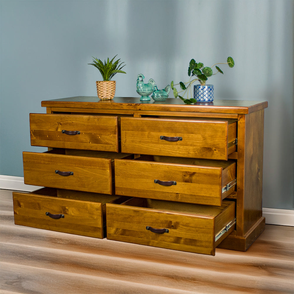 Front view of the Jamaica 6 Drawer Pine Lowboy with its drawers open. There are two potted plants and two blue glass ornaments on top.
