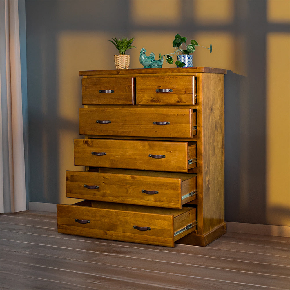 Front view of the Jamaica 6 Drawer Pine Tallboy with its drawers open. There are two blue glass ornaments and two potted plants on top.