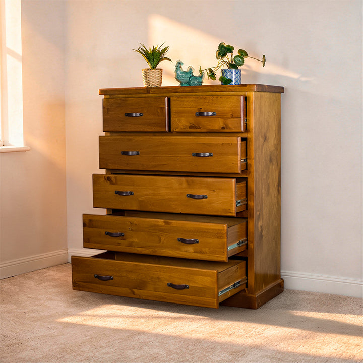 Front view of the Jamaica 6 Drawer Pine Tallboy with its drawers open. There are two blue glass ornaments and two potted plants on top.