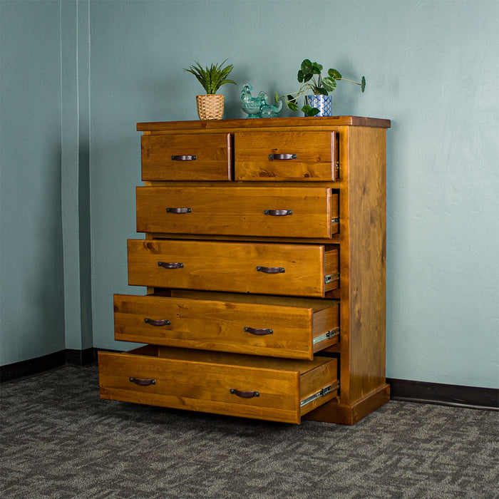 Front view of the Jamaica 6 Drawer Pine Tallboy with its drawers open. There are two blue glass ornaments and two potted plants on top.