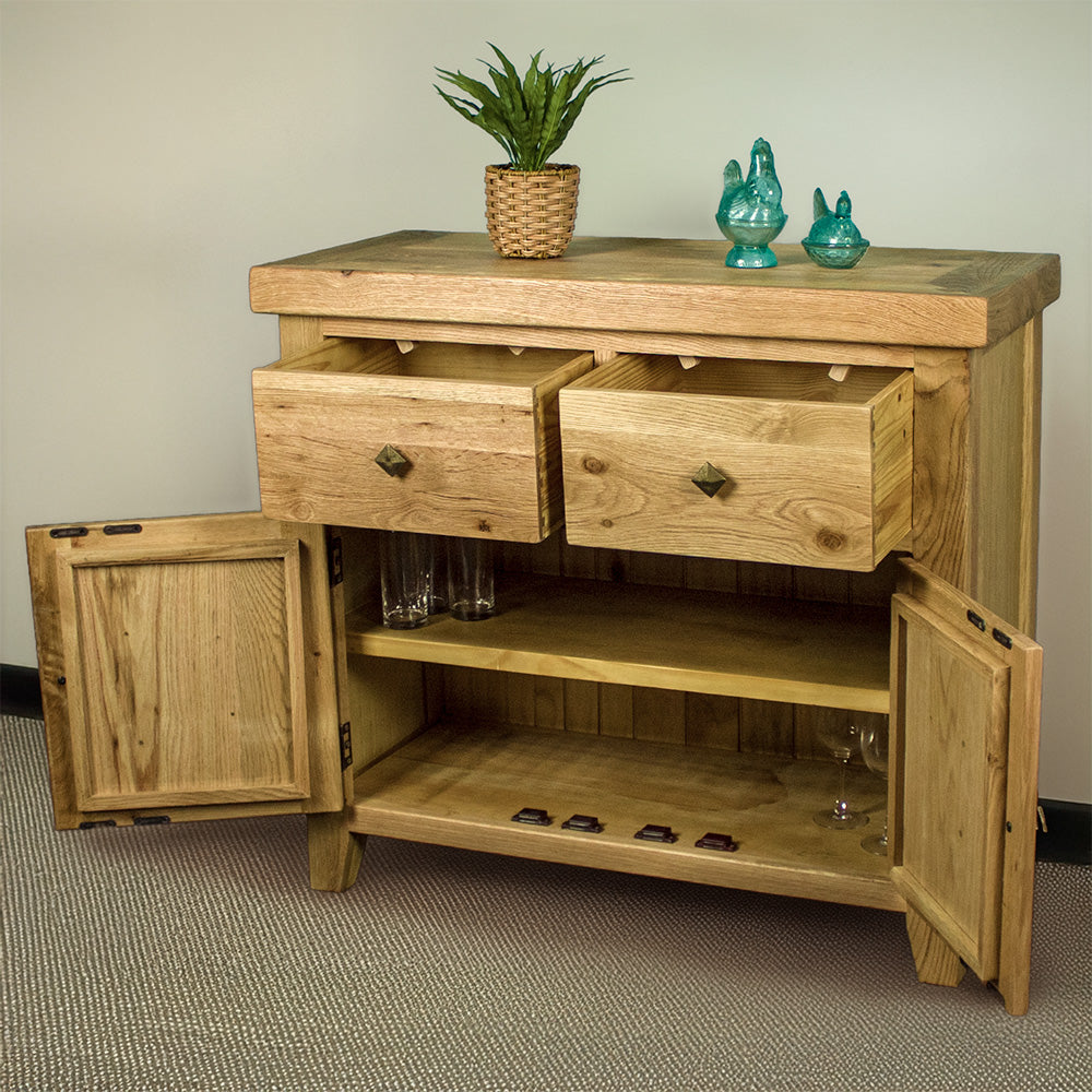 The front of the Maximus Small Oak Buffet with its drawers and doors open. There is a potted plant and two blue glass ornaments on top. There are three glasses on the top shelf, and two wine glasses on the bottom shelf.