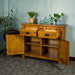 The front of the Rimu stained Montreal 2 Drawer Pine Buffet with its doors and drawers open. There are two potted plants on top, with two blue glass ornaments on top.