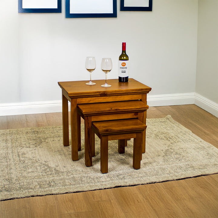 The Montreal 3 Piece Pine Nesting Tables, out from underneath each other. There are two wine glasses and a bottle of wine on the top table.