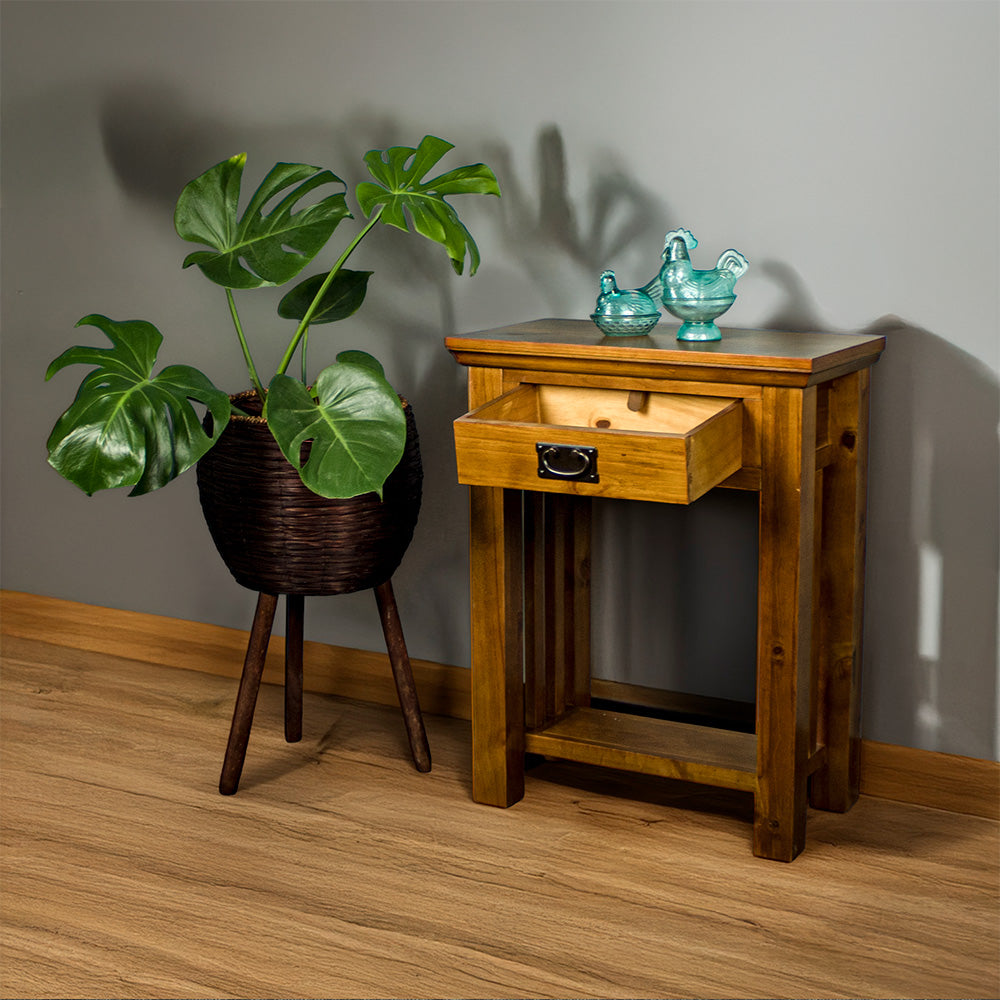 The front of the Montreal Small Pine Hall Table with its drawer open. There are two blue glass ornaments on top with a free standing potted plant next to it.
