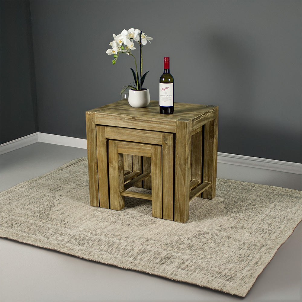 The Vancouver Pine Nesting Tables all underneath the one large table. There is a bottle of wine and a pot of white flowers on top.