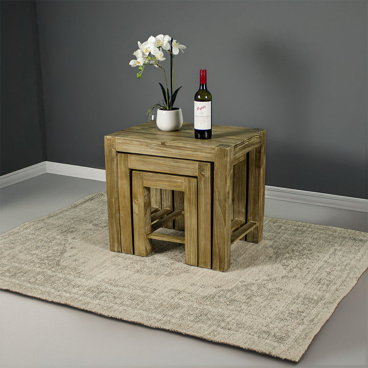 The Vancouver Pine Nesting Tables all underneath the one large table. There is a bottle of wine and a pot of white flowers on top.