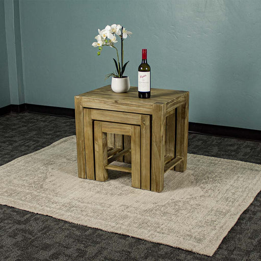 The Vancouver Pine Nesting Tables all underneath the one large table. There is a bottle of wine and a pot of white flowers on top.