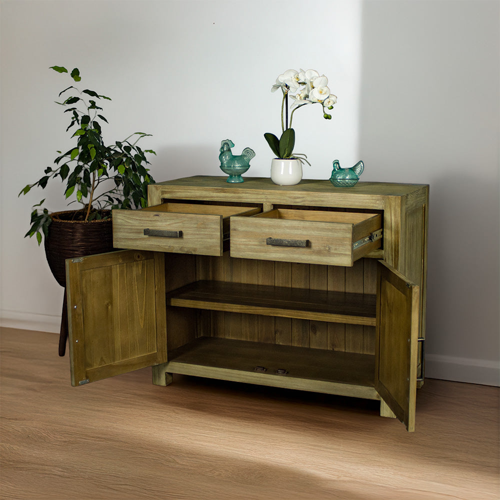 The front of the Vancouver Pine Buffet with its doors and drawers open. There are two blue glass ornaments on top with a pot of white flowers in between. There is a free standing potted plant next to the buffet.