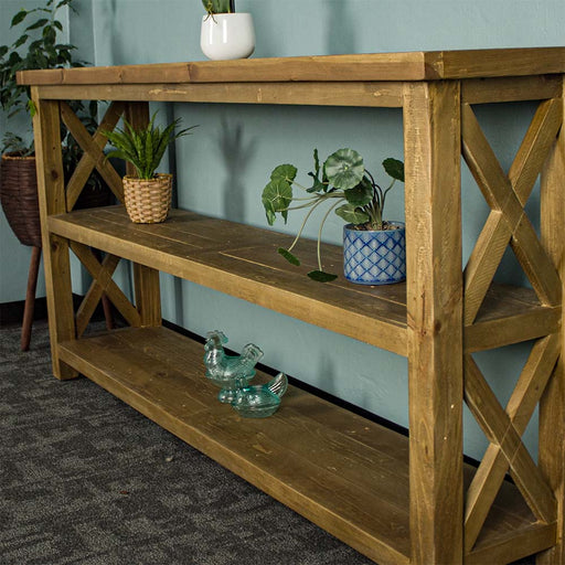 A side-on view of the Ventura Recycled Pine Large Hall Table. There are two equidistant potted plants on the middle shelf and two blue glass ornaments on the bottom shelf.
