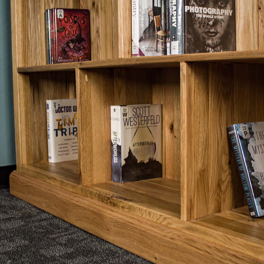 The lower shelf on the Versailles Outback Oak Three Level Bookcase. There are various books on the shelves.