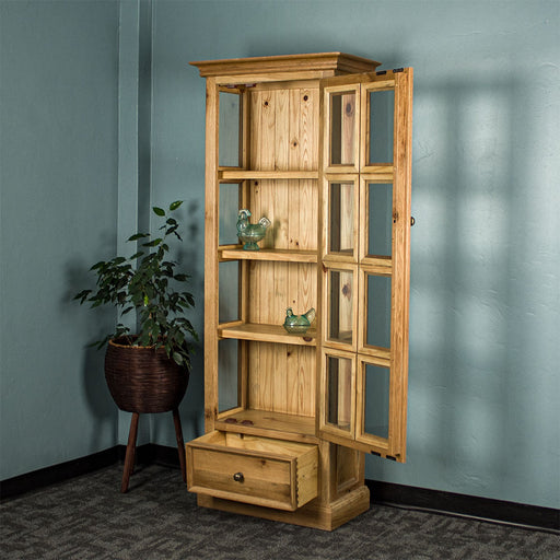 The Versailles Small Display Cabinet with its door and drawer open. There are two blue glass ornaments on the middle two shelves. There is a tall, free standing potted plant next to the cabinet.