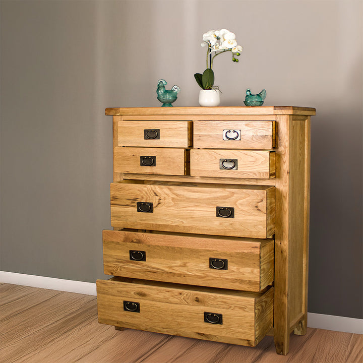 The front of the Vienna 7 Drawer Oak Tallboy with its drawers open. There are two blue glass ornaments on top with a pot of white flowers in between. 