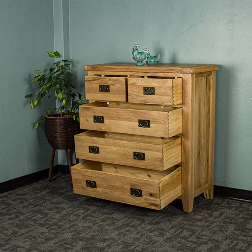 The front of the Yes Five Drawer Oak Chest with the drawers open. There are two blue glass ornaments on top, with a free standing potted plant next to the tallboy.