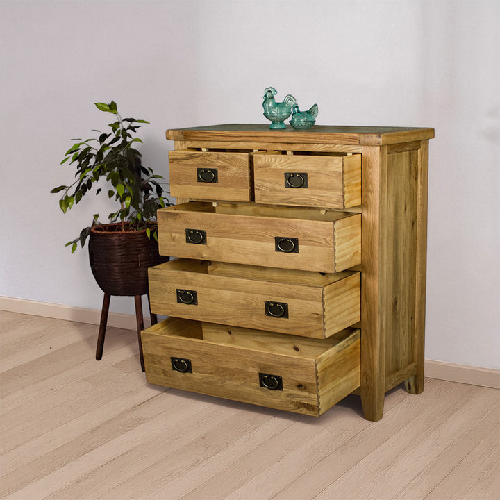 The front of the Yes Five Drawer Oak Chest with the drawers open. There are two blue glass ornaments on top, with a free standing potted plant next to the tallboy.