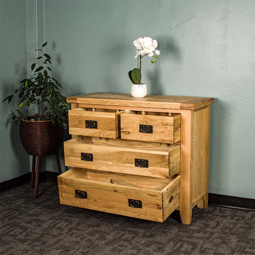 The front of the Yes Four Drawer Oak Lowboy with its drawers open. There is a pot of white flowers on top and a free standing potted plant next to it.