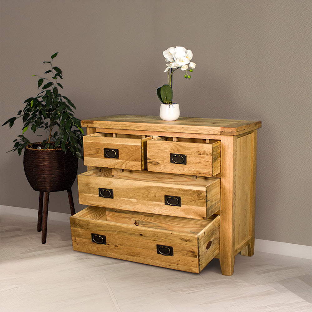 The front of the Yes Four Drawer Oak Lowboy with its drawers open. There is a pot of white flowers on top and a free standing potted plant next to it.