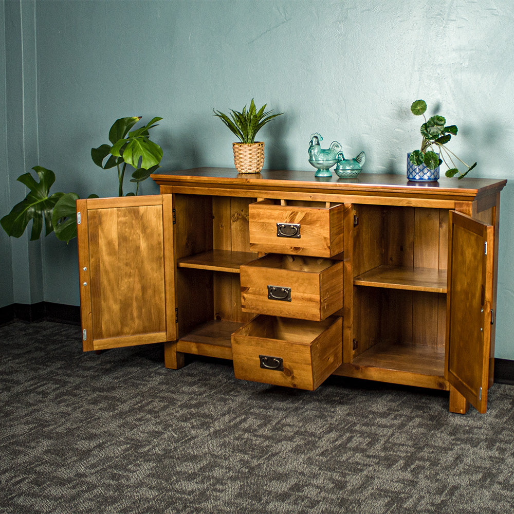 The front of the Montreal Midsize NZ Pine Buffet with its drawers and doors open. There are two potted plants on top with two blue glass ornaments in between.