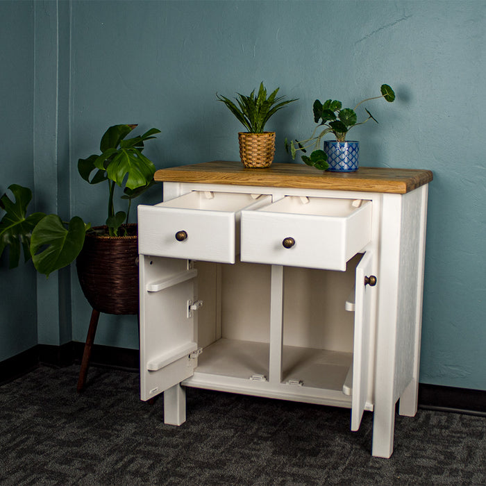 The front of the Loire Small Oak Buffet with its doors and drawers open. There are two potted plants on top with a free standing potted plant next to the sideboard.