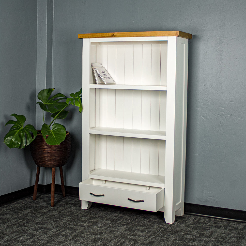 The front of the Felixstowe Pine Bookcase with its drawers open. There are two DVDs on the top shelf. There is a free standing potted plant next to the bookcase.