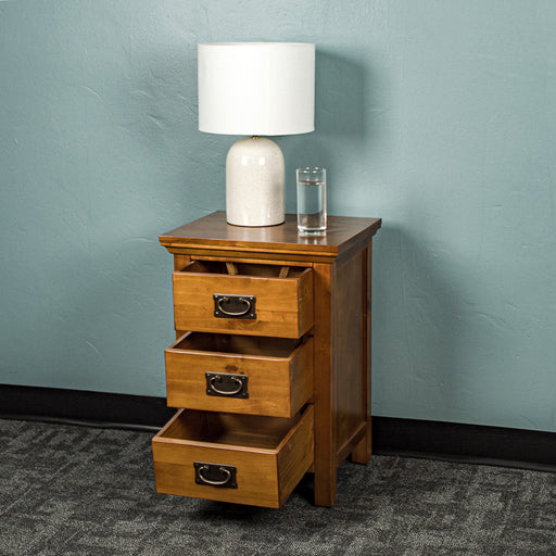 The front of the Montreal Pine Bedside Cabinet with its drawers open. There is a lamp and a glass of water on top.