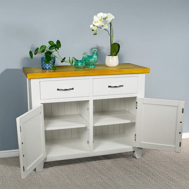 The front of the Felixstowe Small Pine Buffet (White) with its doors open. There are two potted plants with two blue glass ornaments in between them on top of the sideboard.