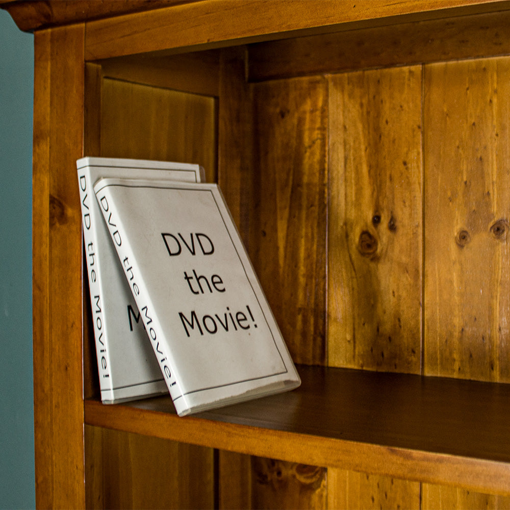 A close view of the shelf on the Montreal Large Pine Bookcase. There are two DVDs in view.