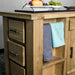 A view of the corner of the Camden Granite Top Kitchen Workbench. There are two hand towels hanging on the towel rail. Two platters of fruit can be seen on the top of the unit.