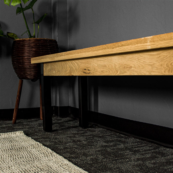 A view down the side of the Golden Gate Long Oak Bench. There is a potted plant at the end.