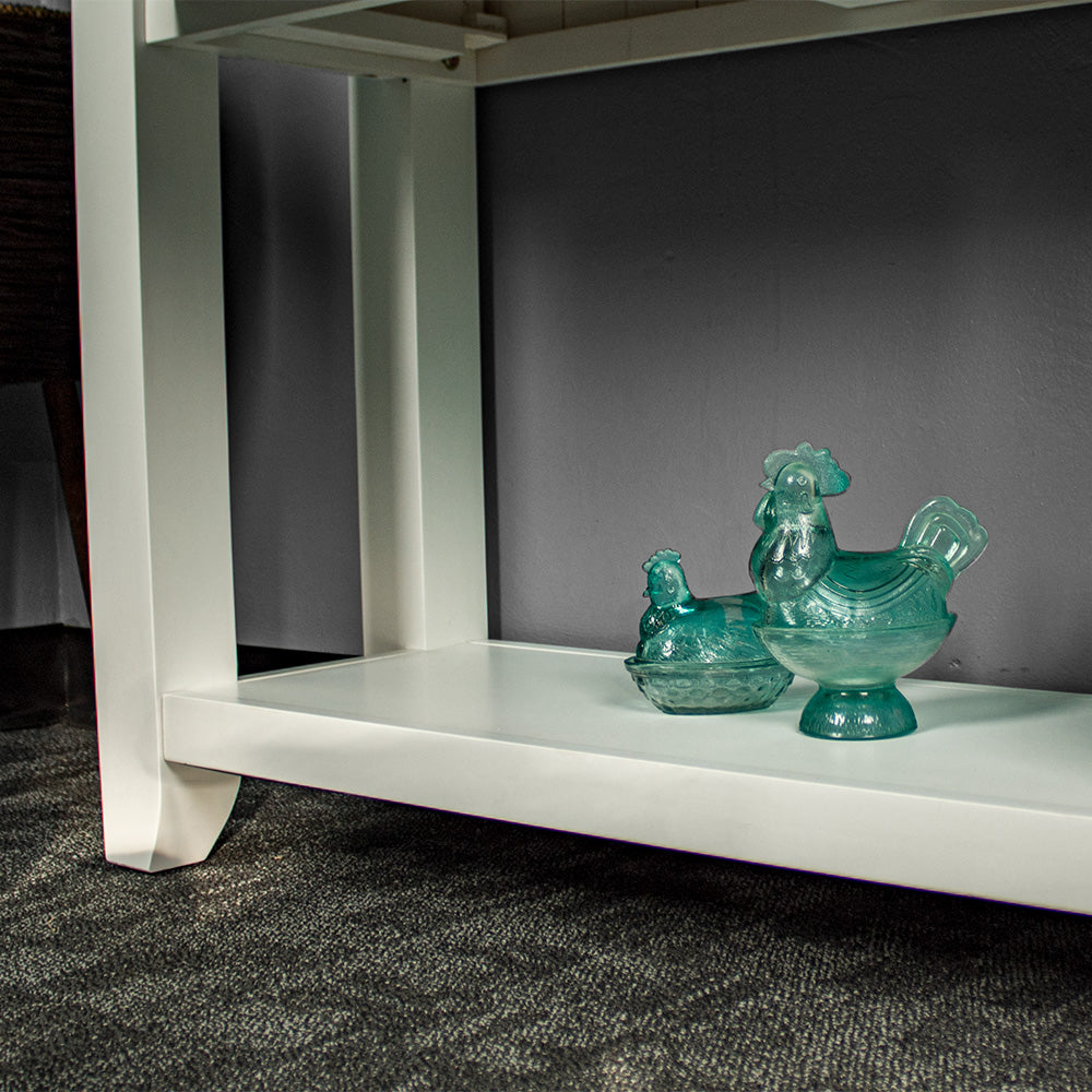 A closer view of the lower shelf on the Felixstowe Large Pine Hall Table. There are two blue glass ornaments in the shape of chickens on the shelf.