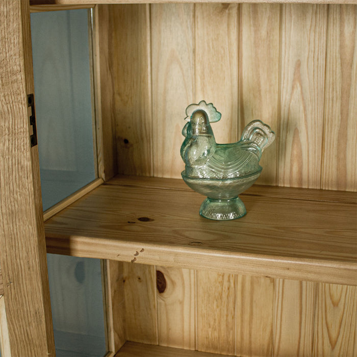 A view of the shelf on the Vienna Oak Glass DIsplay Cabinet. There is a blue glass ornament in the shape of a chicken on display.