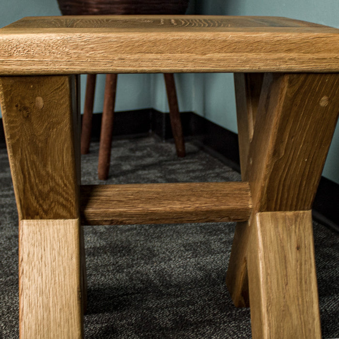 The smaller Amstel Oak Nesting Table from the side, with cross legs and a support bar in the middle.