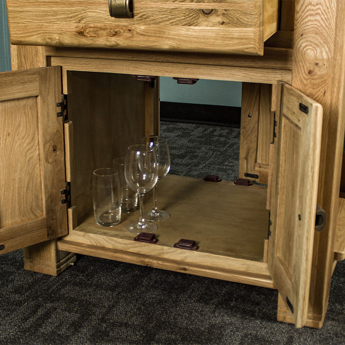 An overall view of the lower shelf of the Danube Compact Granite Top Oak Kitchen Island, which has two sets of glasses and wine glasses next to each other.