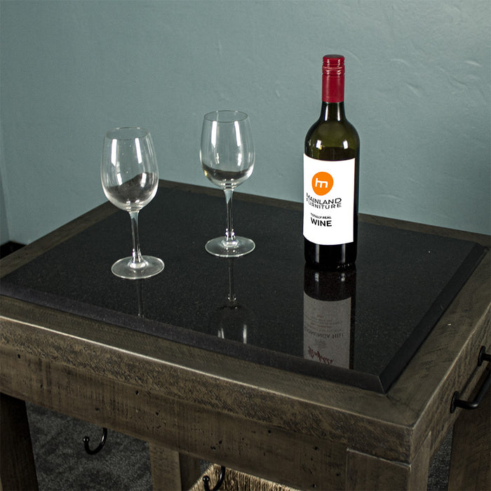 Overall view of the granite top of the Stonemill Recycled Pine Granite Workbench. There are two glasses on top, and a glass bottle next to them. The black metal hooks and handle are also in view.