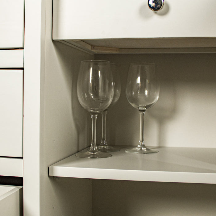 Close up of the shelf of the white Alton 2 Door 5 Drawer Buffet. There are some glass drinking cups.