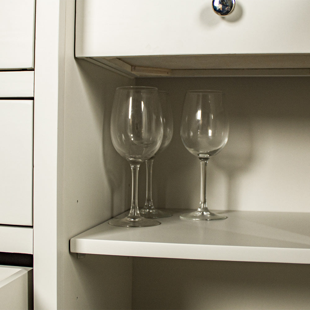 Close up of the shelf of the white Alton 2 Door 5 Drawer Buffet. There are some glass drinking cups.