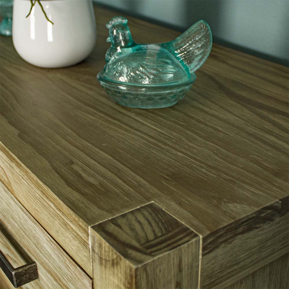 A close up of the top of the Vancouver 6 Drawer NZ Pine Tallboy, showing the wood grain and colour. There is a blue glass ornament in the shape of a chicken on top.