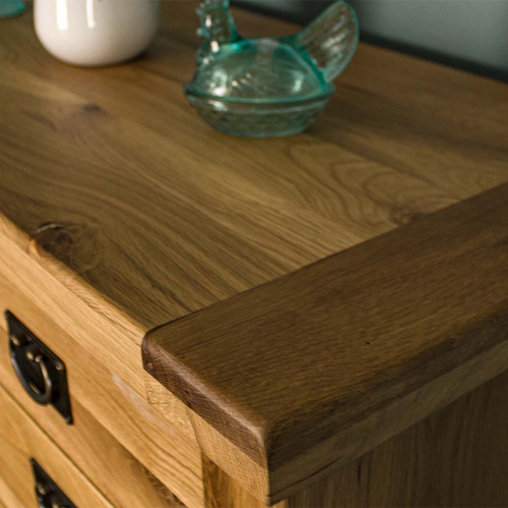 A close up of the top of the Vienna 7 Drawer Oak Tallboy, showing the wood grain and colour. There is a blue glass ornament in the shape of a chicken on top.