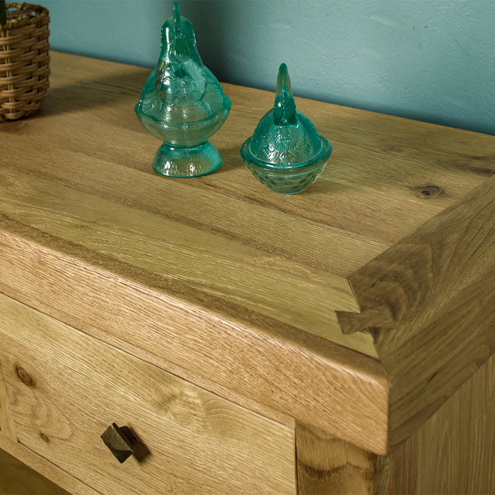 A close up of the top of the Maximus Small Oak Buffet, showing the wood grain and colour. There are two blue glass ornaments in the shape of chickens on top.