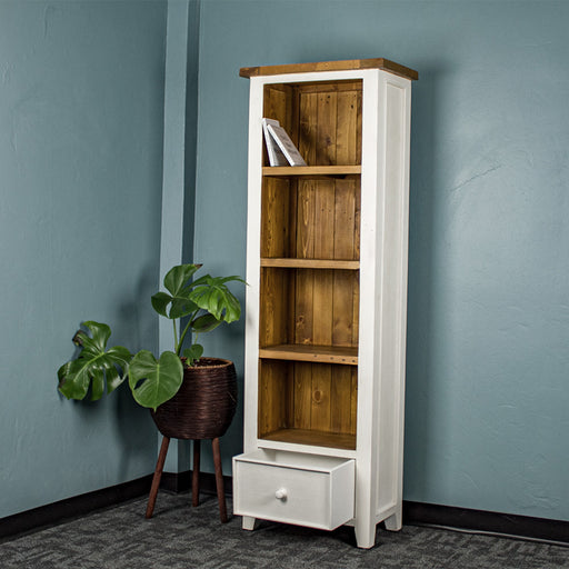 The Tuscan Recycled Pine Tall Bookcase, which as a white exterior and a pine-brown interior and shelving, as well as a brown top. The bookshelf has its singular drawer at the bottom open.
