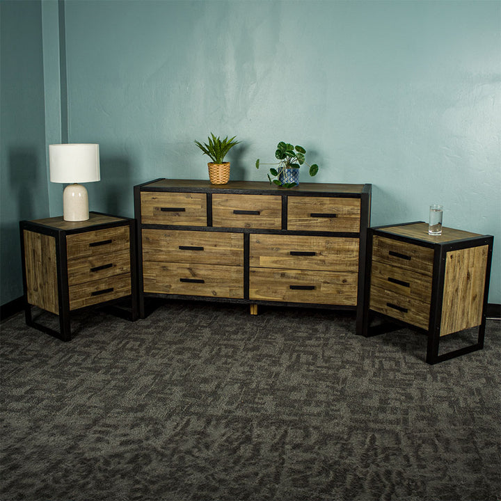 The Victor 7 Drawer Lowboy with two Victor 3 Drawer Bedside Cabinets on either side. There are two potted plants on top of the lowboy and a lamp on the left bedside, and a glass of water on the right bedside.