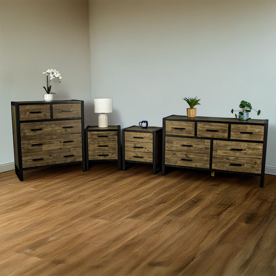 From left to right: Victor 5 Drawer Tallboy, two Victor 3 Drawer Bedside Cabinets and a Victor 7 Drawer Lowboy. There is a small pot of flowers on the tallboy, a lamp on the left bedside, a blue coffee mug on the right bedside, and two potted plants on the lowboy.