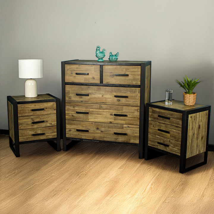 The Victor 7 Drawer Tallboy with two Victor 3 Drawer Bedsides on either side. There are two blue glass ornaments on top of the tallboy, a lamp on the right bedside and a glass of water and potted plant on the right bedside.