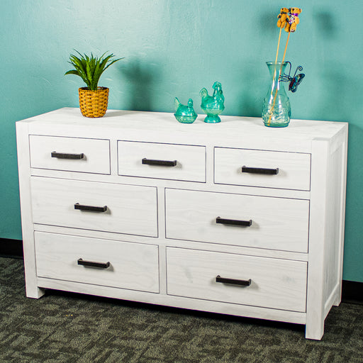 The front of the Vancouver 7 Drawer White Lowboy. There is a potted plant and three blue glass ornaments on top.
